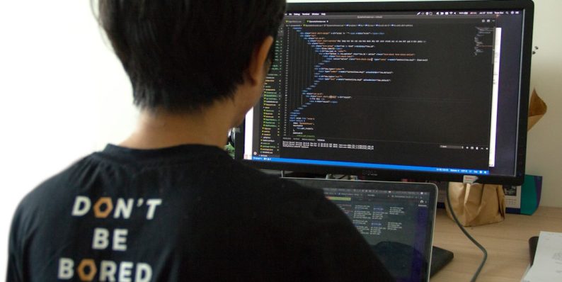 man in black shirt using laptop computer and flat screen monitor developers working, coding teamwork, programming languages