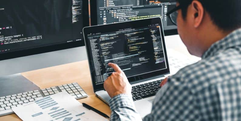 Full Stack Developer working on a laptop, coding with multiple screens displaying frontend and backend tools.