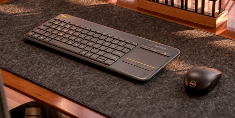 a computer keyboard and mouse on a desk brown leather sleeve office desk apple laptop