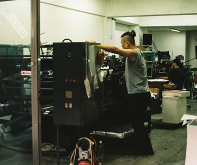 a man standing in front of a machine in a room behind the scenes, factory tour, team working