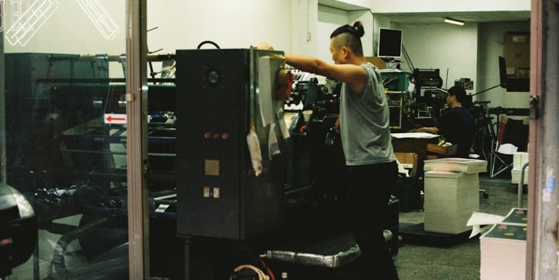 a man standing in front of a machine in a room behind the scenes, factory tour, team working