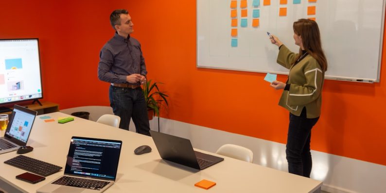 a man and a woman standing in front of a whiteboard startup team meeting, hiring strategy, office culture