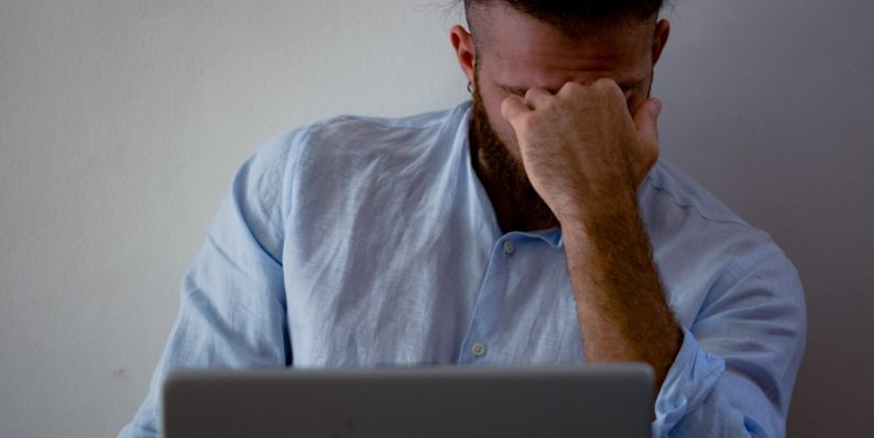 man in blue dress shirt holding silver macbook buffering video frustrated user wifi