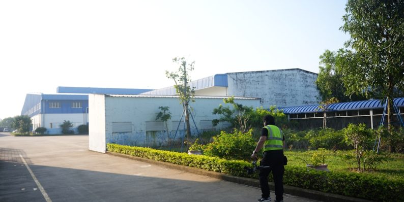 A person in a vest stands near industrial buildings. futuristic factory, cnc operator, acrylic technology