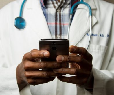 person wearing lavatory gown with green stethoscope on neck using phone while standing telemedicine, wearable tech, digital health