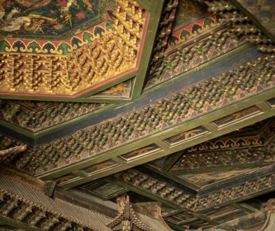 Intricately painted ornate ceiling with detailed patterns. ancient manuscript palm leaf, meditation posture, temple interior